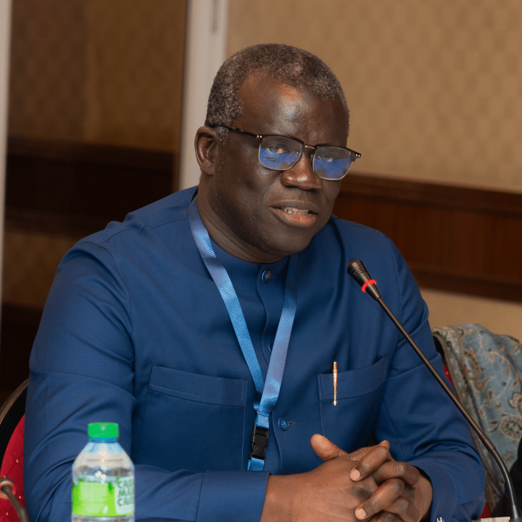 Homme en costume bleu et cravate rayée rouge et blanche parlant à un podium, avec des drapeaux en arrière-plan, dont celui de la Roumanie.